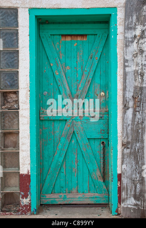 Eine alte grüne Tür verbirgt unbekannte Eigenschaft in einem verlassenen Gebäude in Fort Sumner, New Mexico. Stockfoto