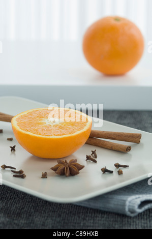 Ganze und halbe Orange mit Zimtstangen und Sternanis auf Teller, Nahaufnahme Stockfoto