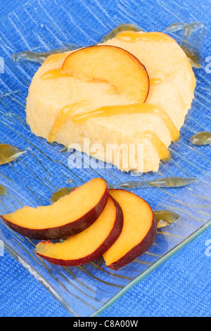 Herzförmige Pfirsich Bayerische Creme-Dessert mit Pfirsich-Sauce und Pfirsich Scheiben auf einer transparenten Glasplatte auf einem blauen Hintergrund. Stockfoto