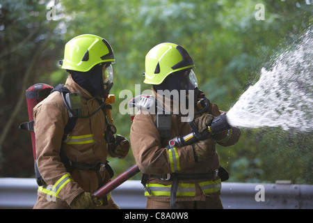 Feuerwehrleute mit einem Schlauch tragen von Atemschutz, UK Stockfoto