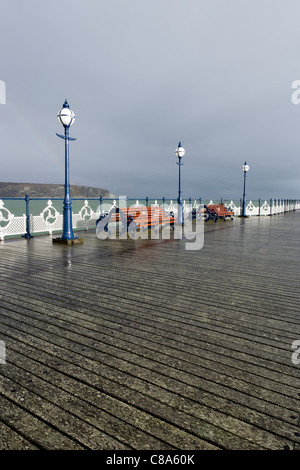 Laternenmasten und einen Sitzplatz mit einem Regenbogen im Hintergrund Swanage Pier nach einem Regenschauer. Stockfoto