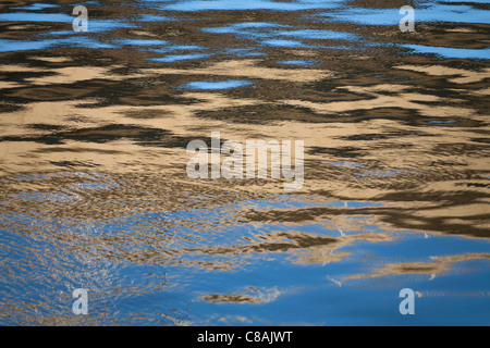 Reflexionen im beweglichen Flusswasser erstellen abstrakte Muster in braun und blues Stockfoto