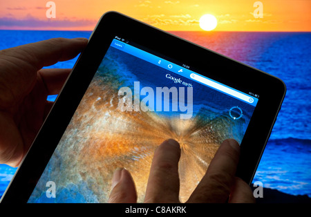 Touchscreen Apple iPad mit Finger auf Touchscreen zoomen Smart Tablet mit Google Earth Anwendung auf dem Display, Sonnenuntergang und Meer im Hintergrund, Stockfoto