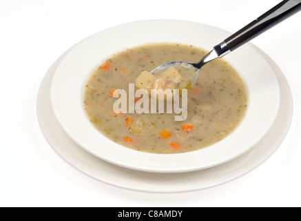 Eine Schüssel mit Kartoffel-Lauch-Suppe mit Löffel Suppe auf weißem Hintergrund. Stockfoto