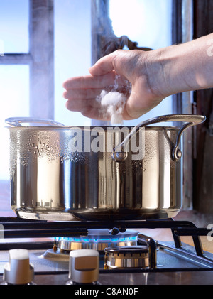 Das Wasser in den Topf auf dem Gasherd hinzufügen eine kleine Handvoll Salz Stockfoto