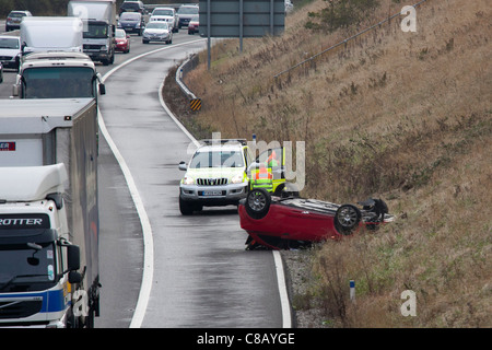 Eine umgekehrte Kfz liegt auf dem Dach auf dem Standstreifen der Autobahn M42 nahe Verzweigung 10. Stockfoto