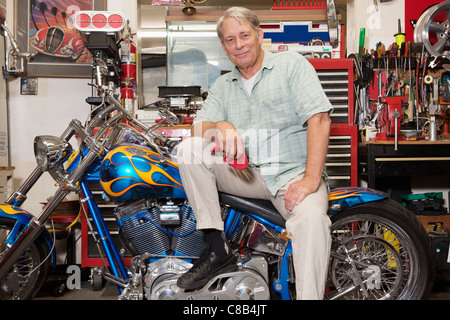 Ältere Mann sitzt auf Motorrad in Werkstatt Stockfoto