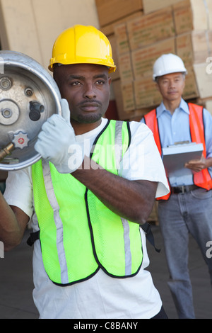 Lagerarbeiter mit Zylinder mit Manager im Hintergrund Stockfoto