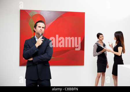 Junger Mann denken mit zwei Frauen reden im Hintergrund in der Kunstgalerie Stockfoto