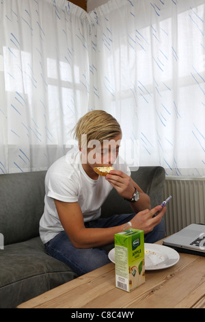 Multitasking-Teenager Umgang mit Frühstück, SMS auf dem iPhone, Macbook Pro, soziale Netzwerke und Hausaufgaben zur gleichen Zeit Stockfoto