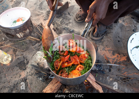 Ein Mann kocht Grüns und Tomaten über dem offenen Feuer in Mongu, Sambia, Südafrika. Stockfoto