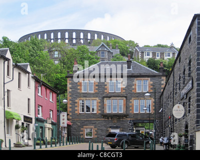 Oban, mit der Brennerei im Vordergrund und McCaig es Tower (oder Dummheit) dominieren den Hügel jenseits. Stockfoto