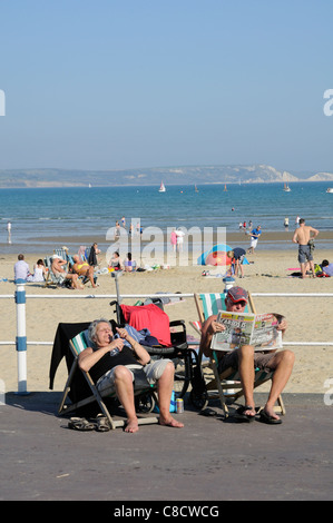 Urlauber sitzen in Liegestühlen am Strand von Weymouth Seaside resort in Dorset England UK Stockfoto