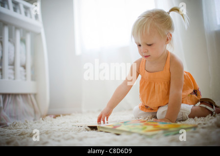 Kleinkind Mädchen sitzen auf Stock mit Blick auf Bilderbuch Stockfoto