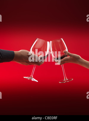 Hände von Mann und Frau halten Gläser Rotwein, toasten, auf rotem Grund Stockfoto
