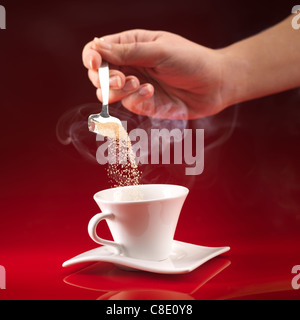 zarte Frauenhand Gießen braunen Zucker in weißen Tasse Kaffee auf rotem Grund Stockfoto