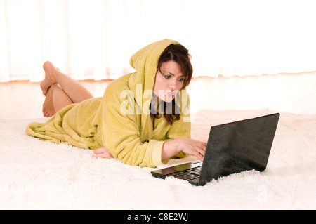 Frau in Robe mit Laptop auf dem Boden liegend Stockfoto