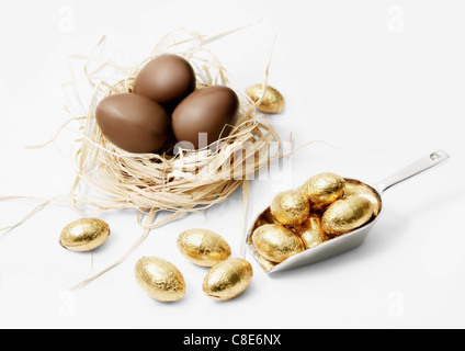 Drei Milchschokolade Eiern in ein Nest und kleinen goldenen Eiern Stockfoto