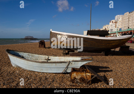 Boote auf einem Kiesstrand am Brighton Seafront mit dem Burn-out-Shell auf dem berühmten West Pier im Hintergrund Stockfoto