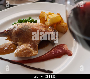 Mahlzeit vergoldet, französische Küche Confit de canard Teller am Tisch im Restaurant mit einem Glas Rot Bordeaux Wein Stockfoto