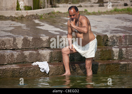 Indisch-hinduistischen Mann Baden und Reinigung seiner Zähne in den Fluss Ganges durch Kshameshwar Ghat in der Heiligen Stadt Varanasi, Indien Stockfoto