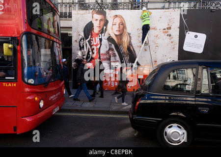 Eine große Mode-Werbung-Plakatwand steht über Verkehr, Fußgänger und Arbeiter passend Lichter auf das Horten. Stockfoto