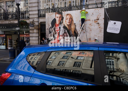 Eine große Mode-Werbung-Plakatwand steht über Verkehr, Fußgänger und Arbeiter passend Lichter auf das Horten. Stockfoto