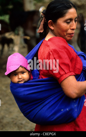 Cusco, Peru. Frau im roten Kleid mit Baby in einem rosa Hut in einem blauen Tuch auf dem Rücken. Stockfoto