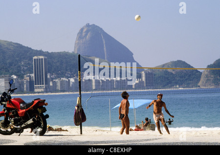 Rio De Janeiro, Brasilien. Junge Männer spielen Sie Volleyball am Strand der Copacabana mit dem Zuckerhut hinter und ein rotes Motorrad. Stockfoto