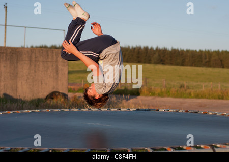 Teenager Springen auf einem Trampolin lachen und dabei Saltos auf einem Sommer Abend im Juli. Stockfoto