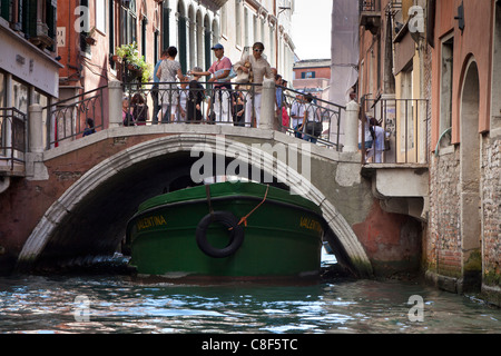 ein Lastkahn vorbei unter einer kleinen Brücke mit Touristen auf der Brücke in Venedig. Stockfoto