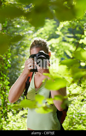 junge Frau trekking zwischen Bäumen und Fotografieren mit Dslr-Kamera. Vertikale Form, Vorderansicht, Hüfte aufwärts Stockfoto