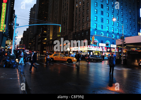 Abenddämmerung Blick Richtung blaues Gebäude West 50th Street, Menschen Kreuzung nassem Asphalt, Taxi drehen 7th Avenue, New York Stockfoto