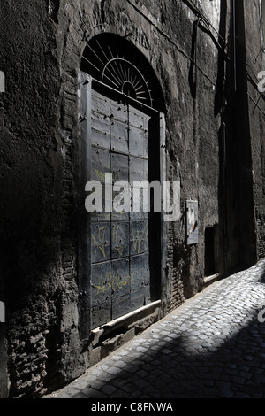 hoher Kontrast Stein texturiert, Wand, gepflasterte Straße mit alten Tor und Tür, in einer Seitenstraße in Trastevere, Rom, Italien Stockfoto