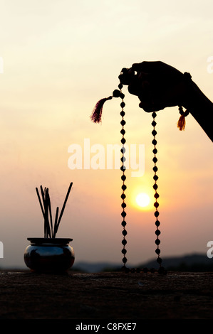 Mans Hand mit indischen Rudraksha / Japa Mala Gebet Perlen und Weihrauch. Silhouette