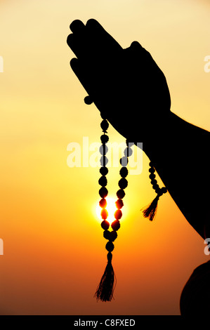 Mans Gebet Hände halten indischen Rudraksha / Japa Mala Gebetskette. Silhouette Stockfoto