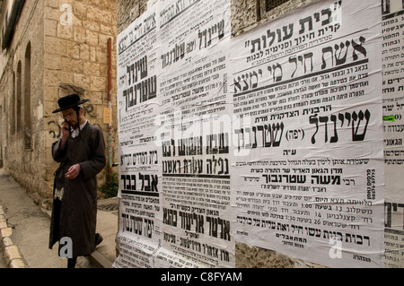 Ein ultra-orthodoxer Jude geht an Paschkvilim vorbei, die auf einer öffentlichen Mauer angebracht sind und als Gemeinschaftsankündigungen im Viertel Mea Shearim dienen, einer ultra-orthodoxen Enklave in West-Jerusalem Israel Stockfoto
