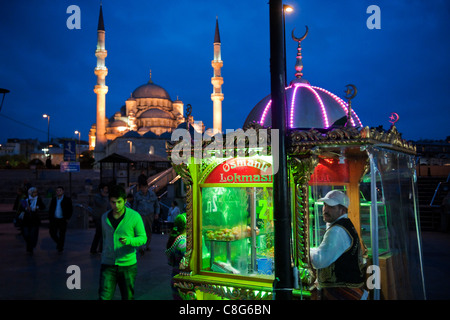 Straßenhändler in der Nacht beleuchtet anschaulich stand außerhalb der neuen Moschee, Istanbul, Türkei mit Menschen zu Fuß durch. Stockfoto