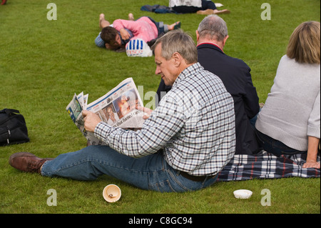 Festival Goer lesen Zeitung entspannen auf der Liegewiese im Sommersonnenschein am Brecon Jazz Festival 2011 Stockfoto