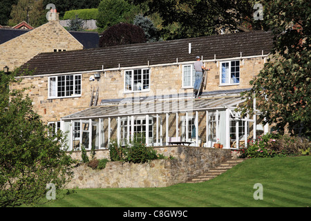 Mann arbeitet auf Leiter über einen Wintergarten für ein Haus in Richmond, North Yorkshire, England Stockfoto