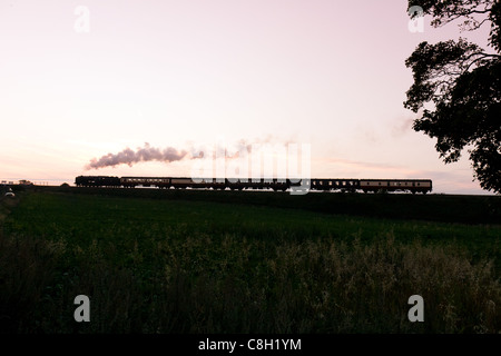 Dampflok zieht einen Personenzug auf der North Norfolk Railway bei Sonnenuntergang Stockfoto