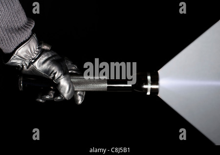 Eine ominöse behandschuhte Hand hält eine Taschenlampe im Dunkeln. Stockfoto