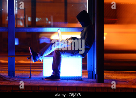 Computer-Benutzer, Hacker, verschwörerisch, außerhalb, Bushaltestelle, mit einem Laptop sitzt. Symbolbild, Computer-Internet-Kriminalität. Stockfoto