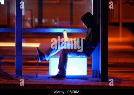 Computer-Benutzer, Hacker, verschwörerisch, außerhalb, Bushaltestelle, mit einem Laptop sitzt. Symbolbild, Computer-Internet-Kriminalität. Stockfoto