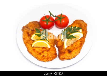 Schnitzel mit Zitronen und Tomaten auf Teller, isoliert auf weißem Hintergrund. Stockfoto