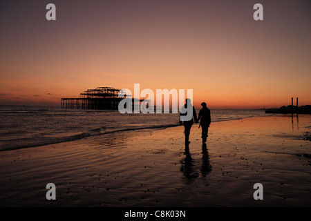 Ein paar hand in hand gehen entlang Brighton Beach, East Sussex, UK zu den Ruinen der West Pier. Stockfoto