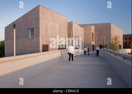 Menschen, die auf einer Fußgängerbrücke durch den Eingang des Kunstmuseums der Hepworth Gallery spazieren (Sonnenbeton außen und blauer Himmel) - Wakefield, West Yorkshire, England, Großbritannien. Stockfoto