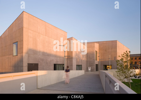 Frau, die auf einer Fußgängerbrücke zum Eingang des Kunstmuseums der Hepworth Gallery spaziert (Sonnenbeton außen und blauer Himmel) - Wakefield, West Yorkshire, England, Großbritannien. Stockfoto