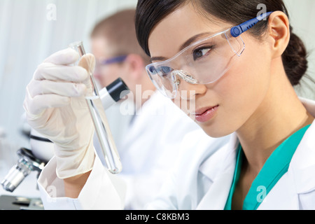 Eine chinesische asiatische medizinische oder wissenschaftliche Forscherin oder Arzt mit Blick auf ein Reagenzglas klare Flüssigkeit in einem Labor Stockfoto