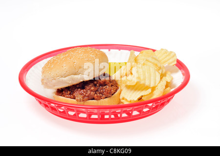 Sloppy Joe Sandwich mit Chips und Pickles auf einem weißen Papierteller in einem roten Retro-Kunststoffkorb auf weißem Hintergrund Ausschnitt. Stockfoto